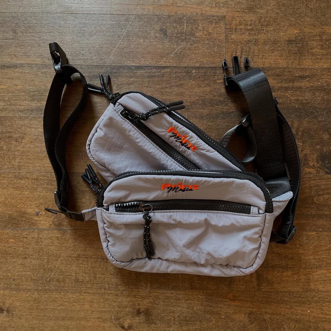 Small gray waist bag with black straps on a wooden surface